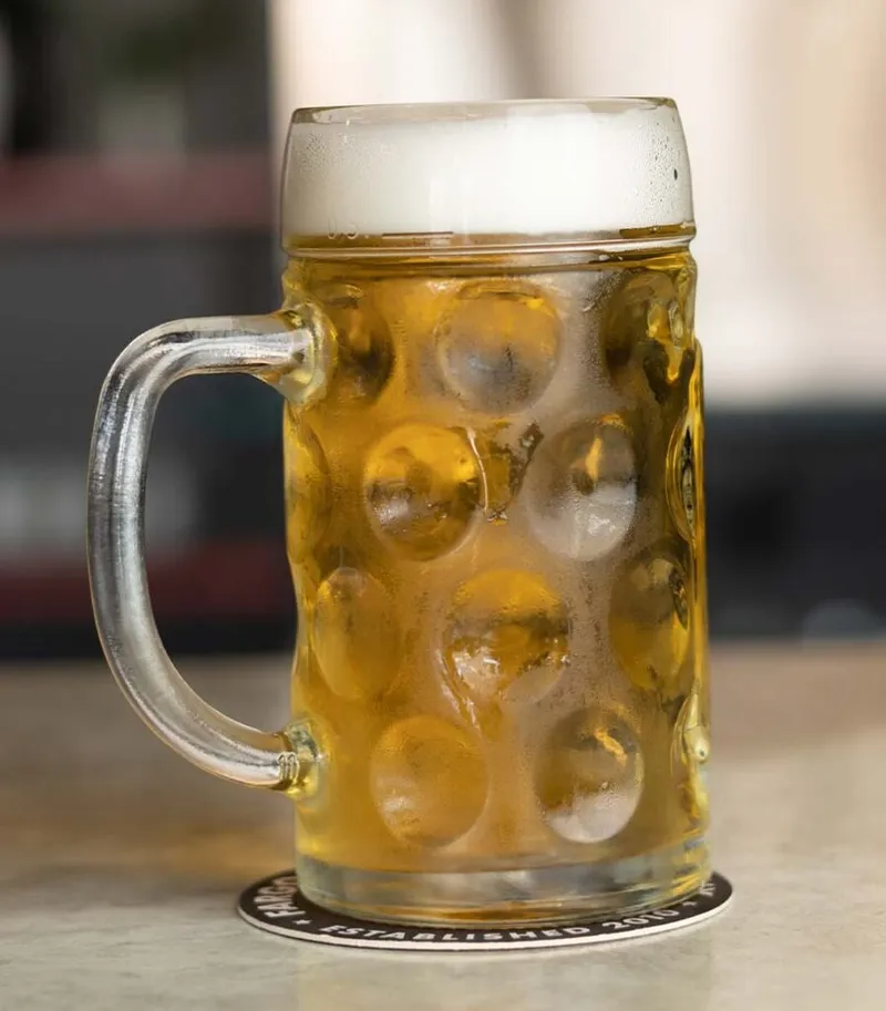 Frothy golden lager in a dimpled glass beer stein on a bar coaster