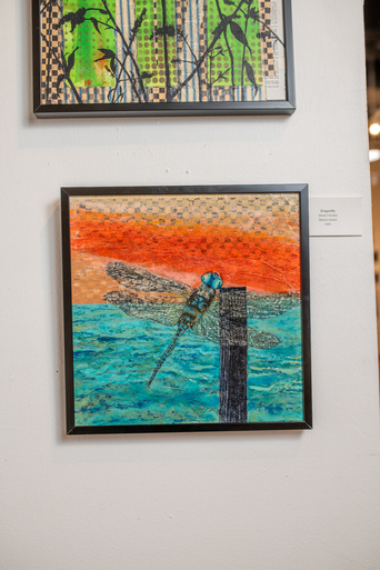 Framed mixed-media artwork of a dragonfly perched on a post against an orange and teal background