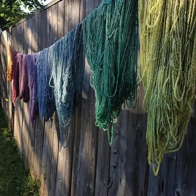 Colorful hand-dyed yarn skeins hanging on a wooden fence outdoors