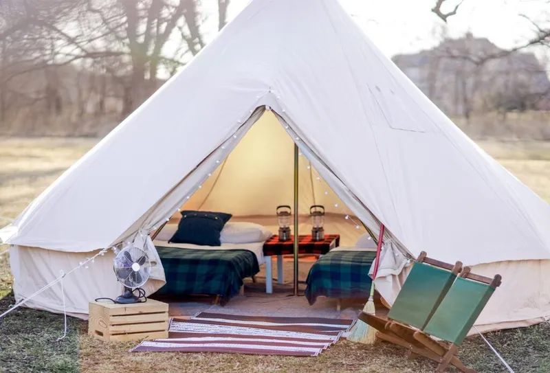 Canvas bell tent with string lights, plaid bedding, and a camp chair outside