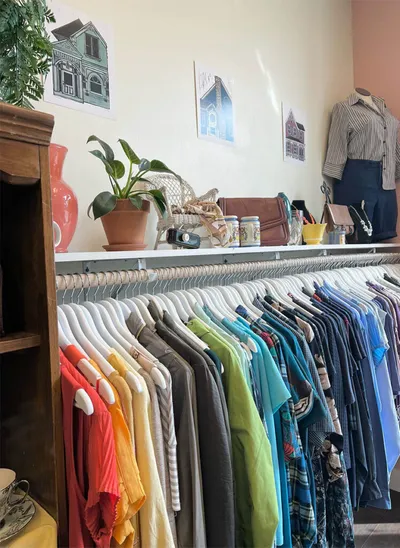 Colorful clothes on a rack inside a small boutique with artwork and a mannequin on the wall shelf
