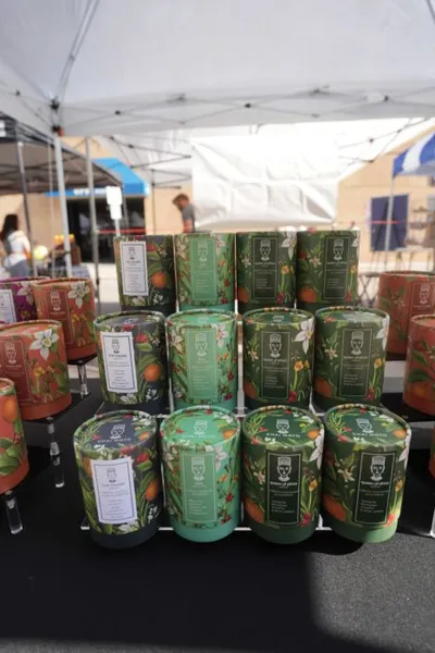 Botanical-printed green candle tins displayed on a table at an outdoor market stall