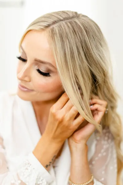 Blonde woman in a white robe adjusting her earring, eyes downcast