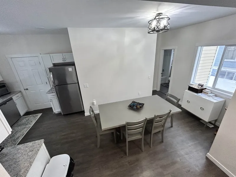Open-plan dining area and kitchen with grey table, four chairs, stainless steel fridge, and dark hardwood floors
