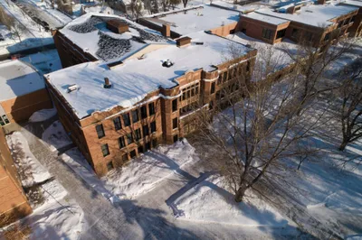 Aerial winter view of a snow-covered red brick university building surrounded by bare trees