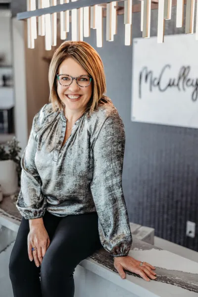 Smiling woman with glasses and blonde bob seated in a modern interior near a McCulley sign