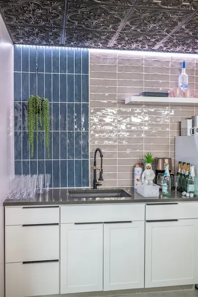 Modern kitchenette with white cabinets, dark faucet, blue vertical tiles, and ornate tin ceiling