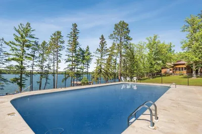 Outdoor pool with lake view framed by tall pines under a blue summer sky
