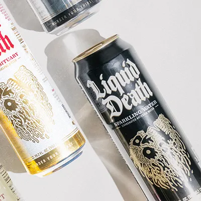 Liquid Death sparkling water black can beside a white can on a light surface