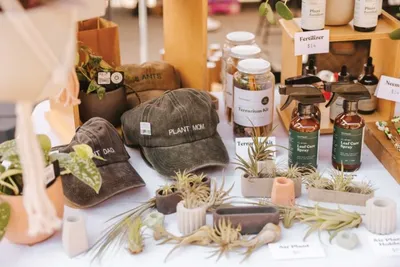Market table display of "Plant Mom" and "Plant Dad" caps, air plants, small succulents, and spray bottles