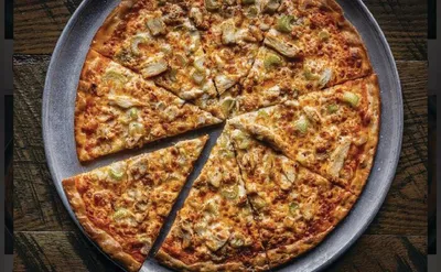 Sliced pizza topped with melted cheese and green peppers on a round metal pan