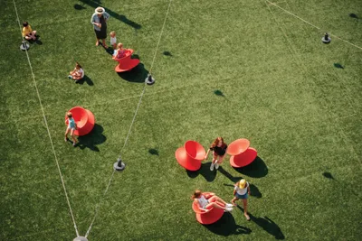 Aerial view of people socializing around large red sculptural chairs on a green lawn