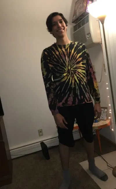 Smiling young person wearing a colorful tie-dye long-sleeve shirt and black shorts