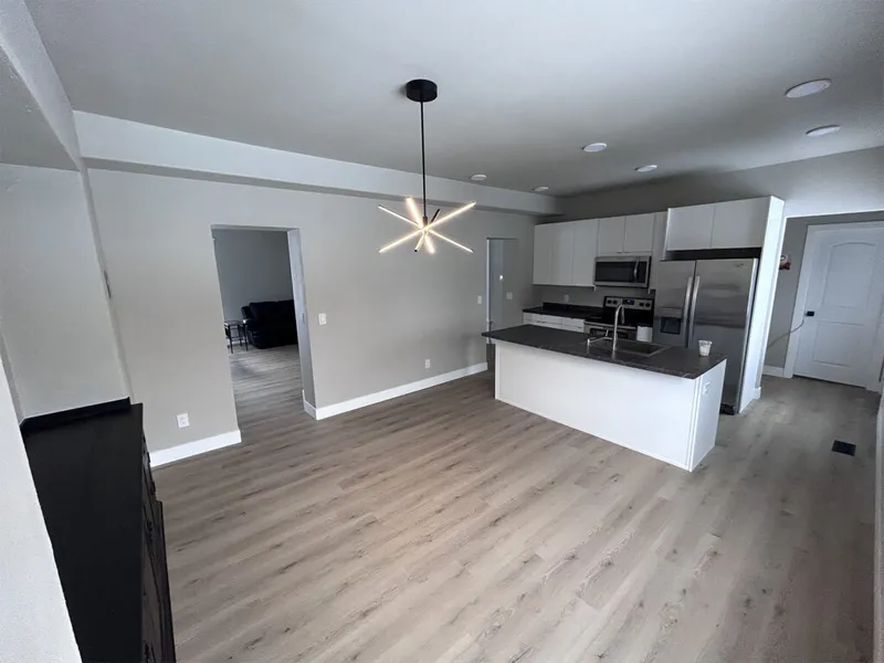 Open-plan kitchen and living area with white cabinets, dark countertops, and a starburst pendant light