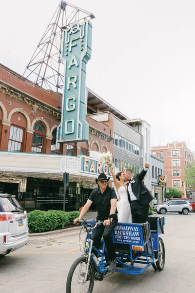 Bride and groom celebrate on a Broadway Rickshaw in front of the Fargo Theatre marquee