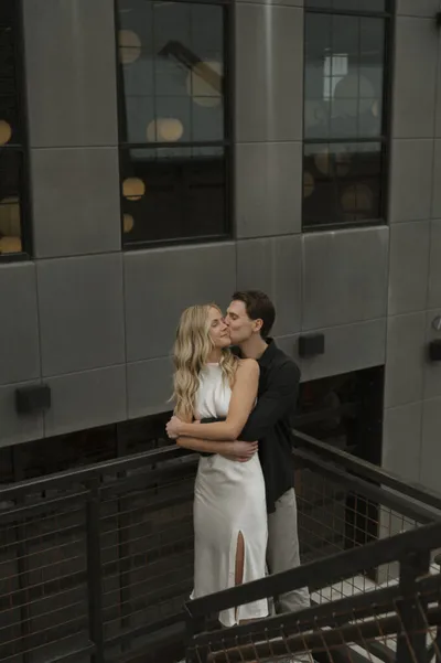 Couple embracing on a metal balcony, woman in white satin dress, man in dark suit