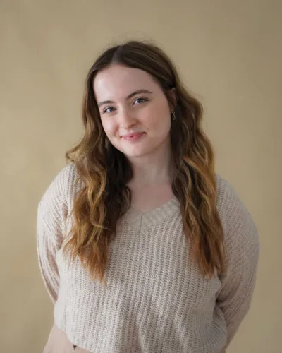 Young woman with long wavy brown ombre hair in a cream knit sweater against a beige background