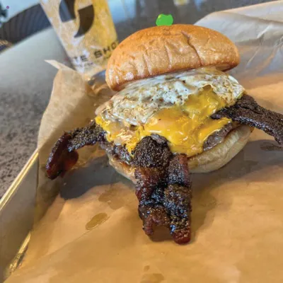 Loaded burger with fried egg, melted cheese, and crispy bacon on parchment paper