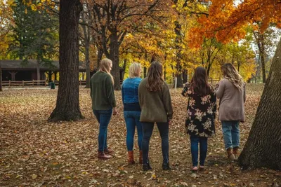 Five women standing together among autumn trees covered in orange and yellow leaves