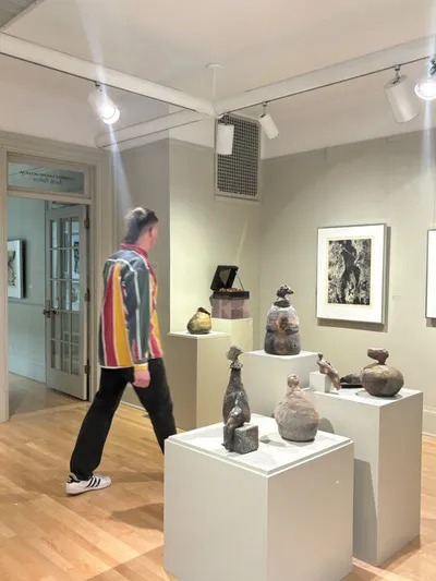 Person in colorful striped jacket walking past ceramic sculptures on white pedestals in a gallery