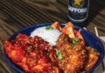 Blue plate of saucy fried chicken with rice and a Sapporo bottle in background