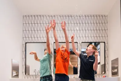 Three boys laughing and reaching arms up toward falling confetti in a bright modern interior