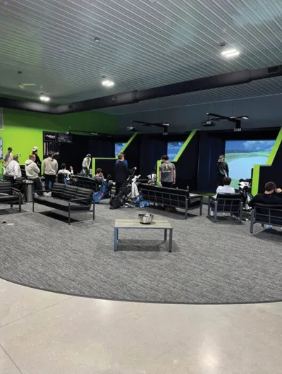 Indoor golf simulator lounge with green walls, seating, and screens showing a golf course