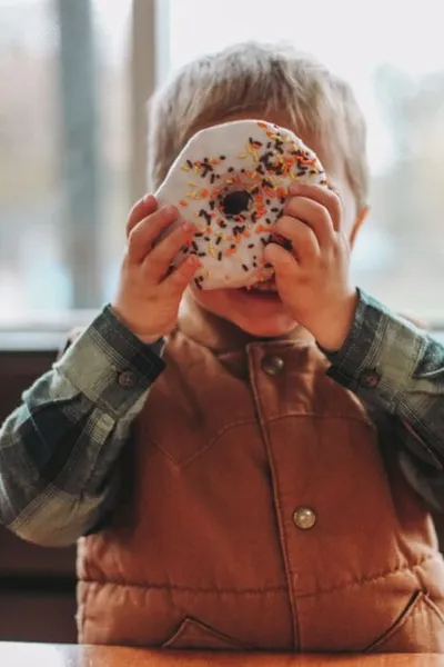 Young boy holding a large white sprinkled donut up to his face