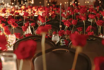 Banquet tables lined with rows of tall-stemmed red roses and candles in a dimly lit event hall
