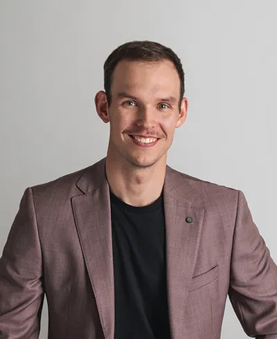 Smiling man in a mauve blazer and black shirt against a gray background