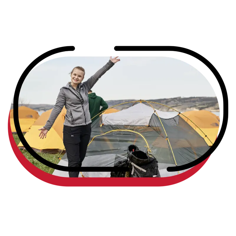Smiling woman in a gray hoodie waving beside a gray and yellow tent at a campsite