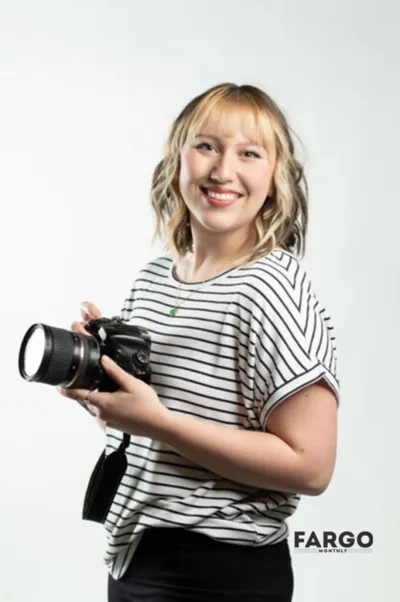 Smiling woman with blonde bob holding a DSLR camera, wearing a striped t-shirt