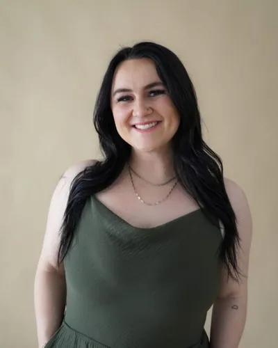 Smiling woman with long dark hair wearing a green tank top and layered necklaces