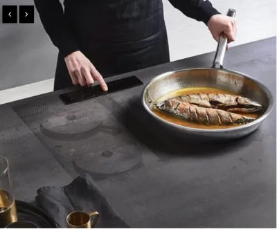 Chef in black holding a pan of whole fish over a dark stone cooktop