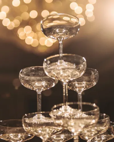 Stacked champagne coupe tower with warm bokeh lights in background