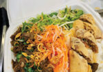 Vietnamese noodle salad with shredded carrots, greens, and fried items in a takeout container