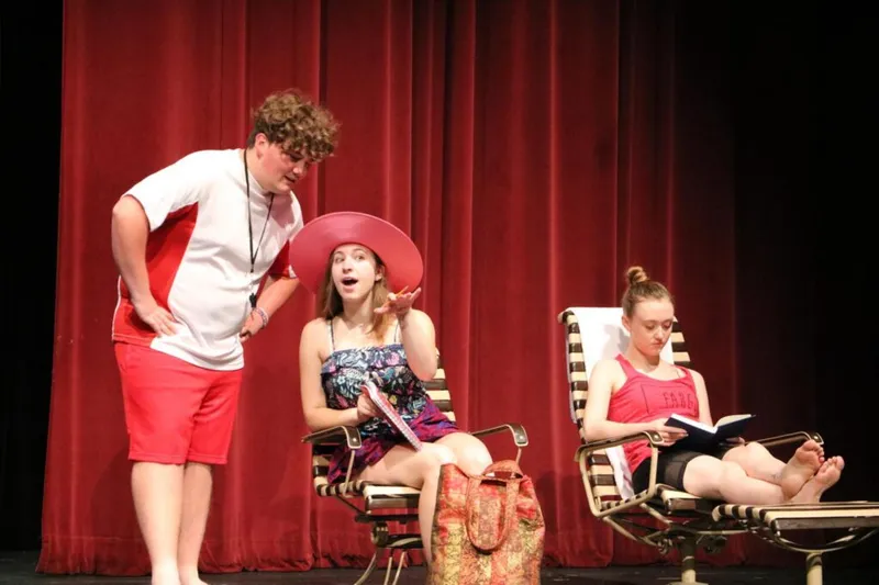 Three young performers on a red-curtained stage in a beach-themed scene