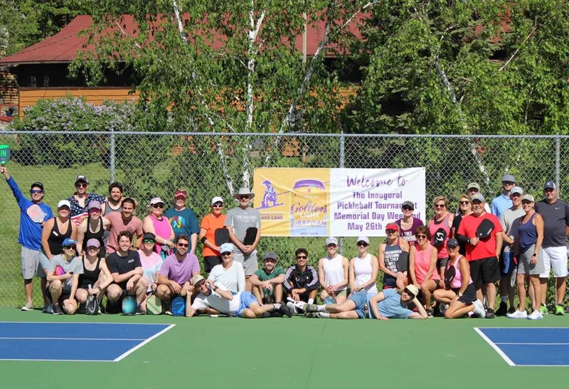 Large group of pickleball players posing on an outdoor court beside an inaugural tournament banner