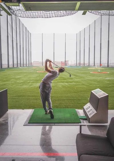 Golfer mid-swing at an indoor driving range bay with green turf and nets
