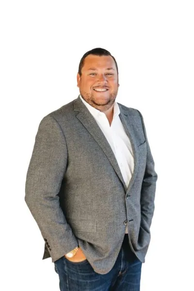 Smiling man in gray blazer and jeans standing against white background