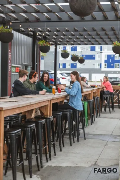 People socializing at long wooden bar-height tables on a covered outdoor patio