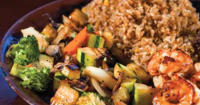 Sizzling shrimp with stir-fried vegetables and fried rice on a dark plate