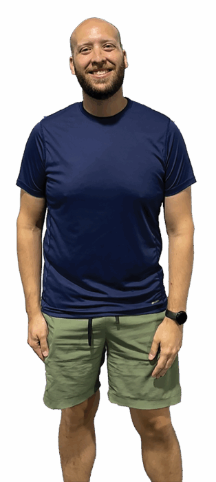Smiling bald man with beard in navy T-shirt and olive shorts standing against white background