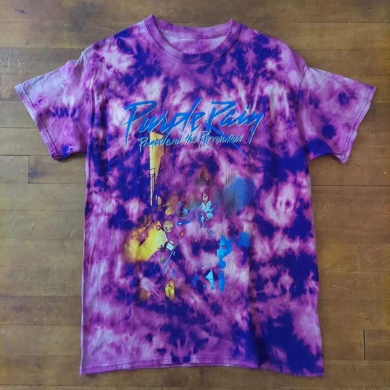 Purple Rain graphic tee with purple and pink tie-dye pattern, laid flat on wood surface