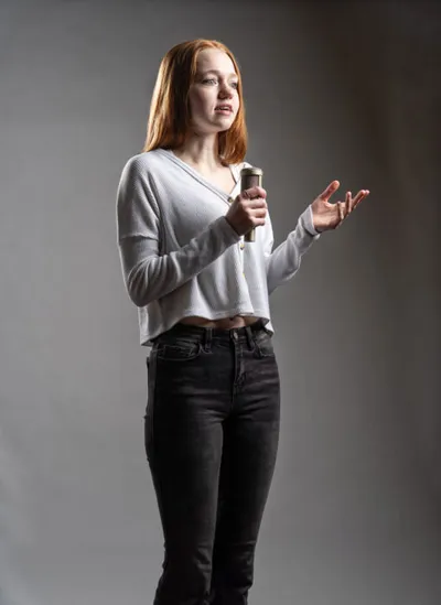 Young woman with red hair holds a microphone and gestures while speaking