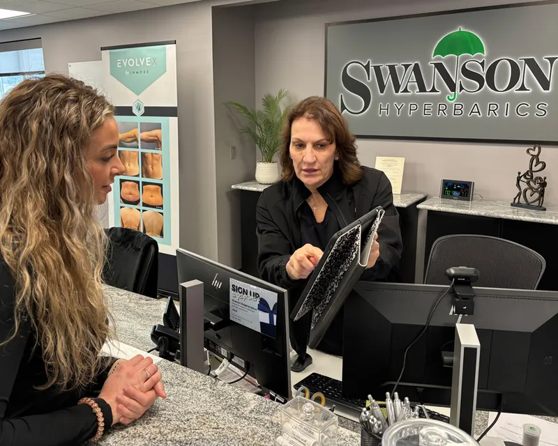 Staff member shows a tablet to a client at the Swanson Hyperbarics front desk
