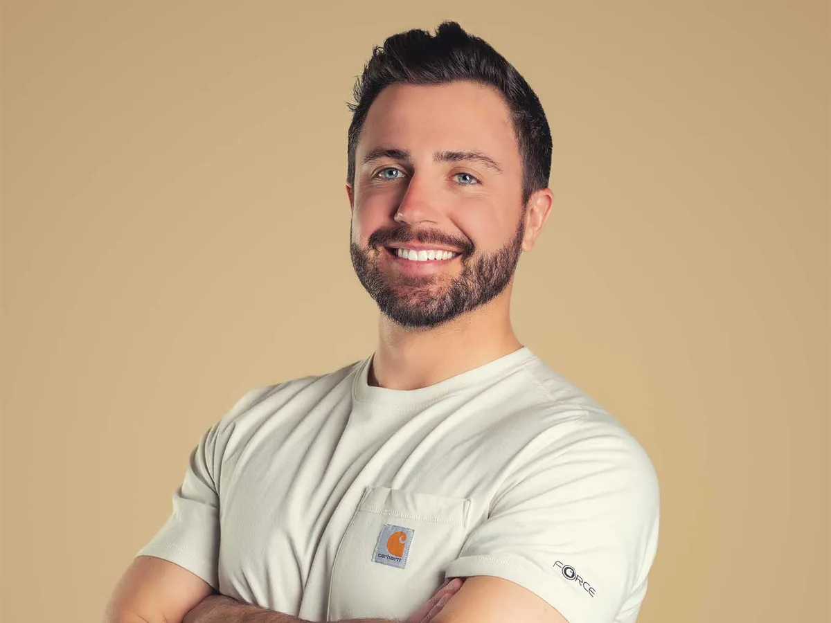 Smiling man with short dark hair and beard, arms crossed, wearing a white Carhartt t-shirt