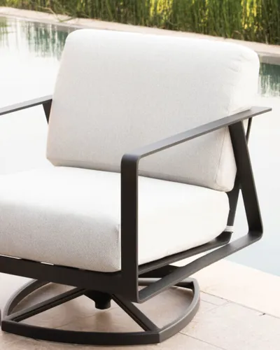 Dark metal swivel lounge chair with white cushions beside a pool