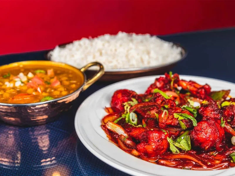 Red-sauced spiced meat on a white plate with dal and steamed rice