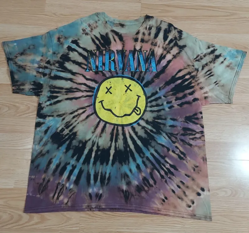 Tie-dye Nirvana graphic tee with spiral black, blue, and purple pattern on wood floor